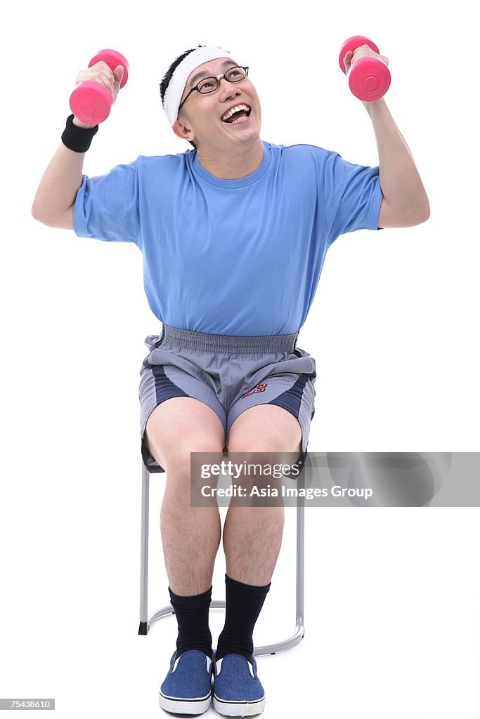 Man sitting on stool, lifting dumbbells