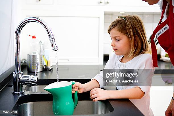 a girl filling a pitcher with water. - jug - fotografias e filmes do acervo