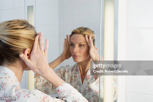 woman smoothing out wrinkles on face with hands - mirror stockfoto's en -beelden