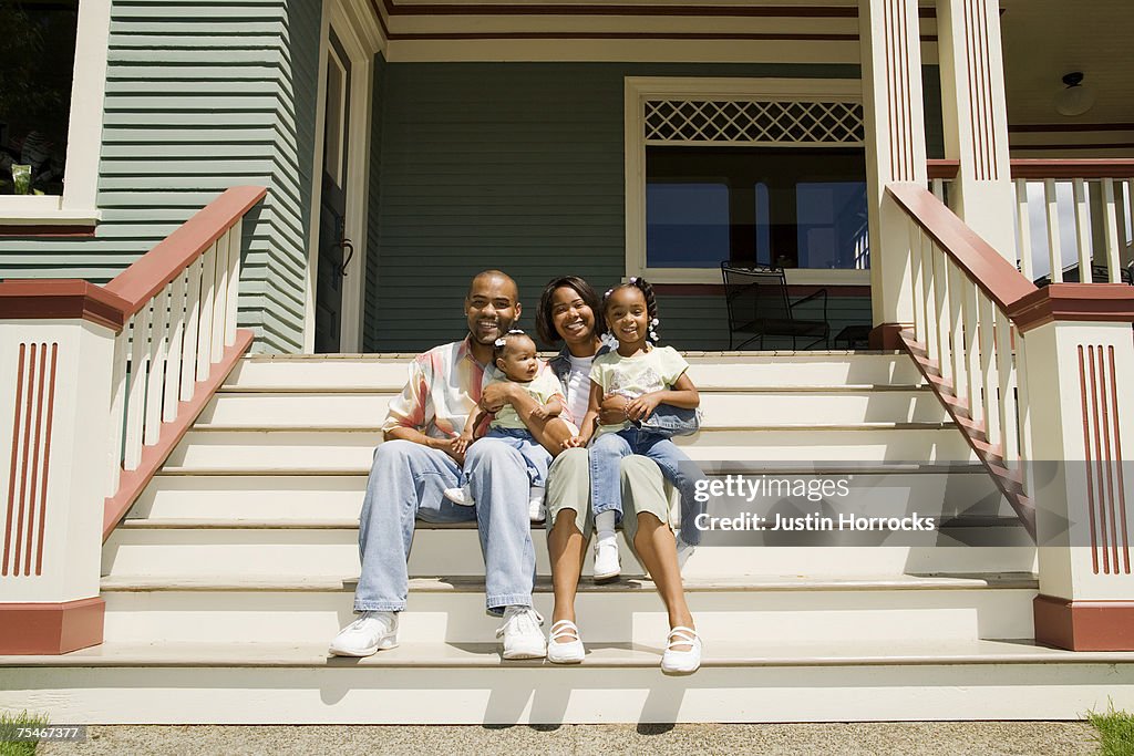 Photo of a young family sitting on the steps in front of their house.