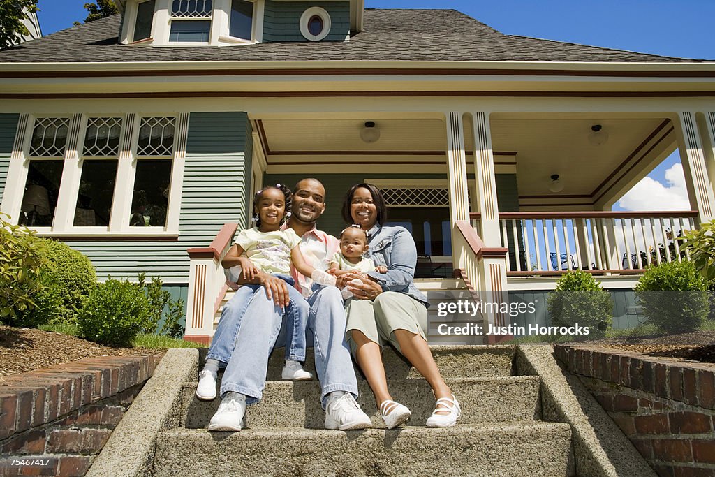Photo of a young family of four sitting on the steps in front of their home.
