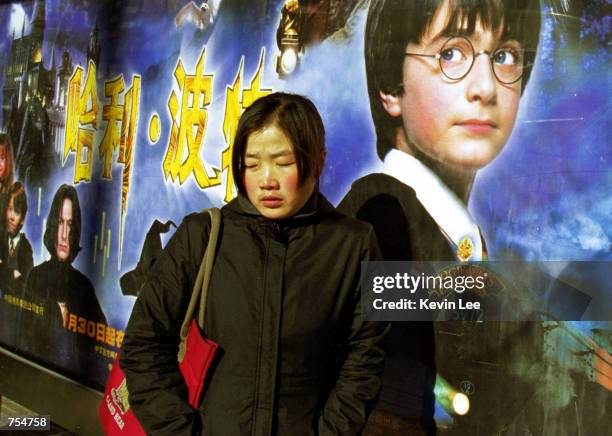 Chinese woman waits at a bus stop next to a billboard featuring the movie, "Harry Potter And The Sorcerer's Stone" January 22, 2002 along a Beijing...