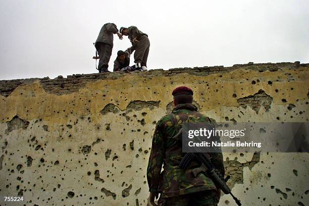 German International Security Assistance Force soldier watches as an eager soccer fan scales a wall February 15, 2002 to enter Kabul's Olympic...