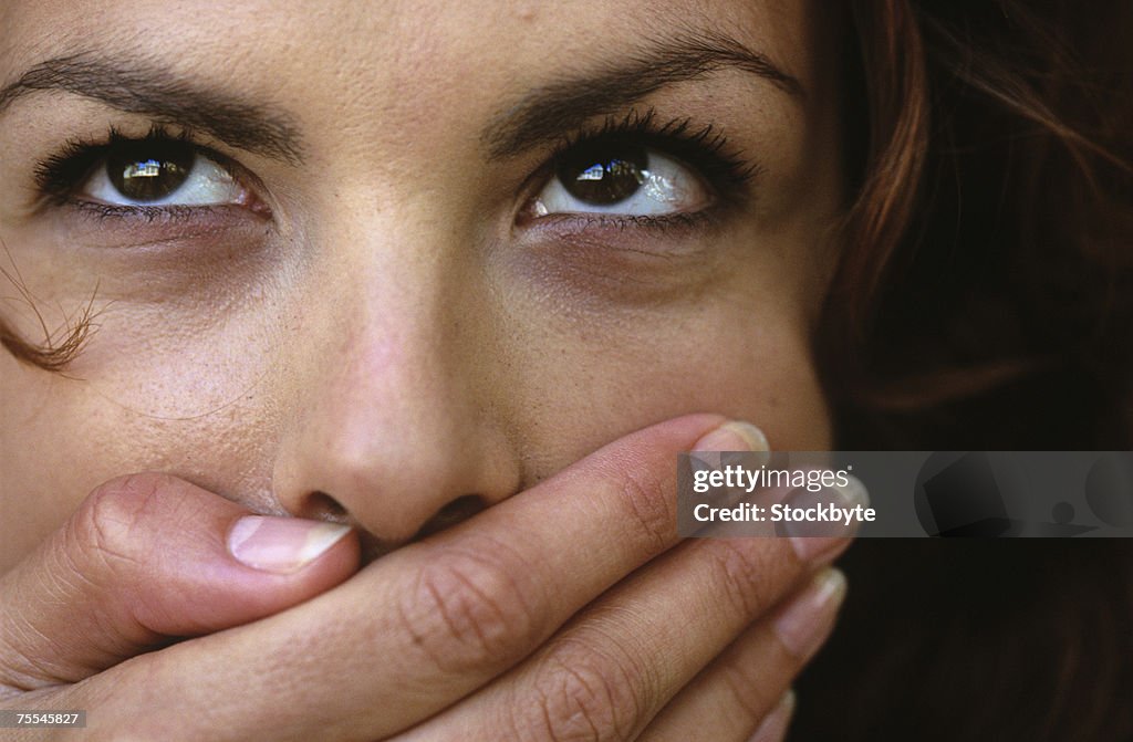 Young woman covering mouth with hand and looking up,close up
