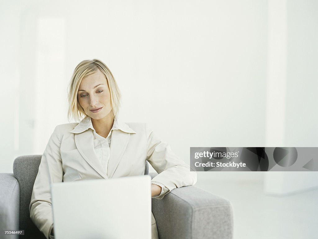Mid adult businesswoman sitting in armchair using laptop,upper half
