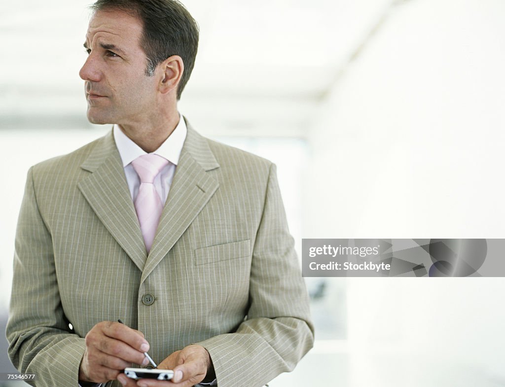 Businessman using palmtop,waist up,looking away