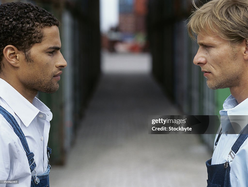 Two young men standing face to face in front of cargo containers,profile