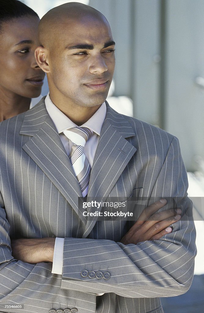 Business man with crossed arms looking aside,woman in background