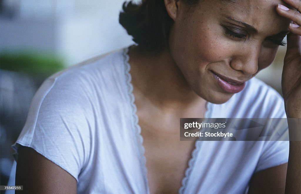 Mid adult woman with hand on forehead,crying,close-up