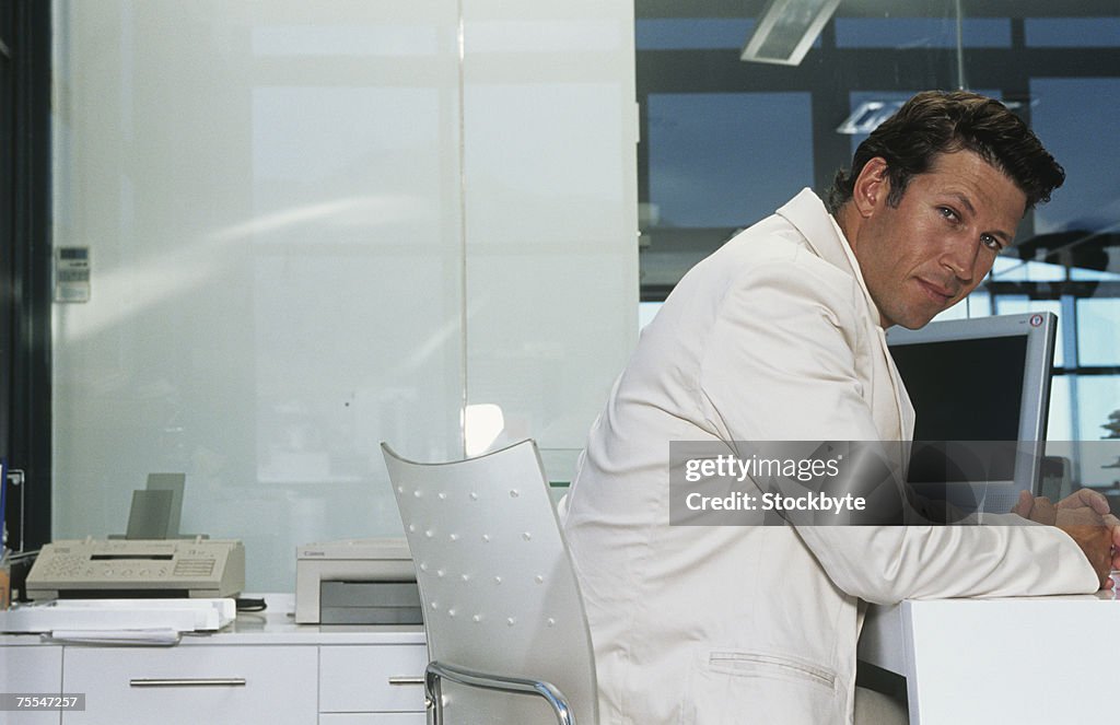 Mid adult businessman sitting at desk in office,side view,portrait