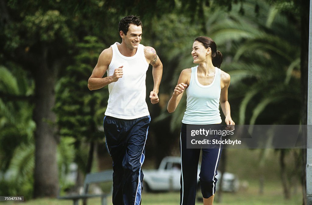 Mid adult man and woman jogging in park,looking in eyes and smiling