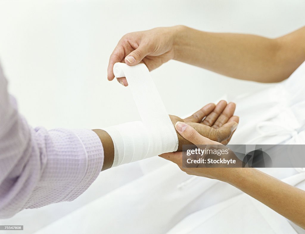 Nurse wrapping bandage around patient's wrist,close-up on hands