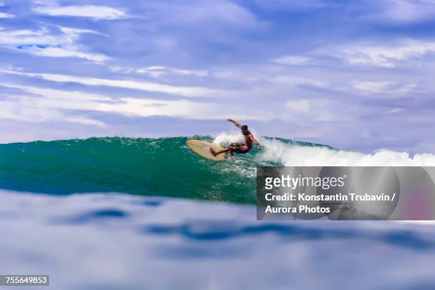 clouds over male surfer riding wave, kuta, lombok, indonesia - kuta stock pictures, royalty-free photos & images