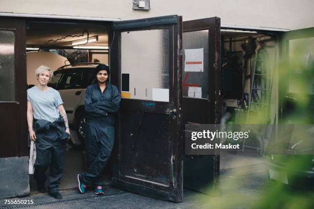 portrait of female mechanics standing at doorway of auto repair shop - auto repair shop background stock pictures, royalty-free photos & images