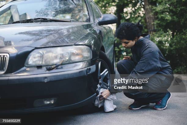 full length of female mechanic cleaning car wheel outside auto repair shop - wheel rim ストックフォトと画像