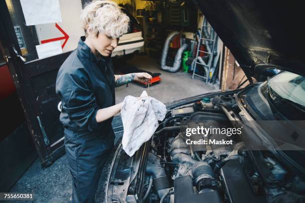 side view of female mechanic checking oil with dipstick outside auto repair shop - resourceful stock pictures, royalty-free photos & images