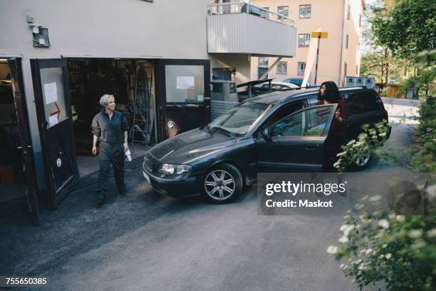 female mechanic looking at customer opening car door outside auto repair shop - auto repair shop exterior stock pictures, royalty-free photos & images