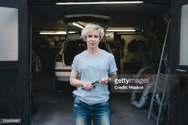 portrait of female owner holding work tool while standing at entrance of auto repair shop - 車　作業員 ストックフォトと画像