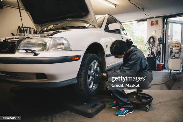 side view of female mechanic examining car wheel at auto repair shop - wheel rim ストックフォトと画像