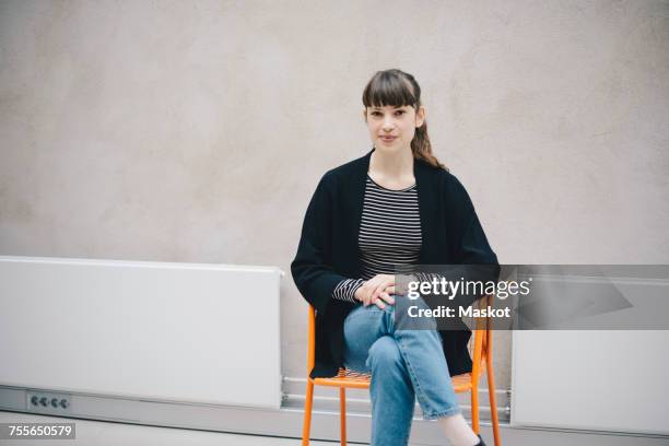 portrait of confident female computer programmer sitting on chair against beige wall in office - abrigo negro fotografías e imágenes de stock