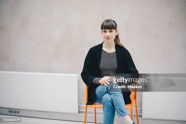 portrait of confident female computer programmer sitting on chair against beige wall in office - black coat bildbanksfoton och bilder