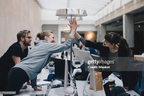 happy female computer programmers giving high-five over desk in office - choque de manos en el aire fotografías e imágenes de stock