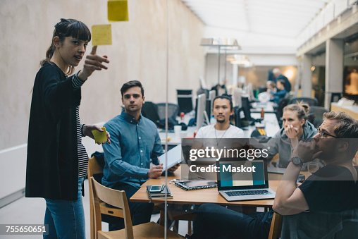 Computer programmer explaining adhesive note while giving presentation to colleagues in office Computer programmer explaining adhesive note while giving presentation to colleagues in office