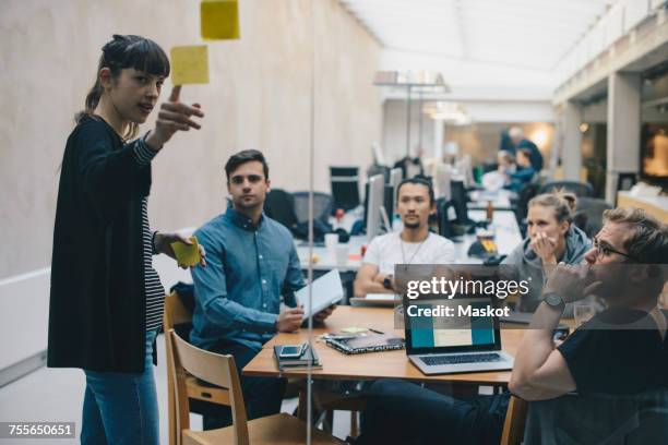 computer programmer explaining adhesive note while giving presentation to colleagues in office - web designer stock pictures, royalty-free photos & images