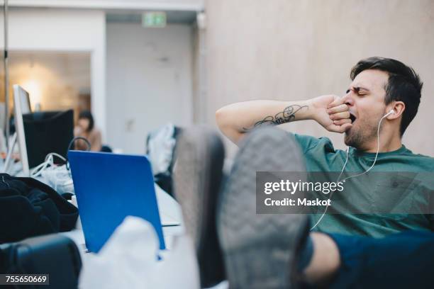 tired computer programmer yawning while sitting with feet up at desk in office - yawning stock photos et images de collection