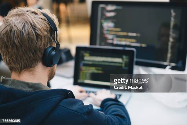 over the shoulder view of businessman wearing headphones while programming on laptop at creative office - webdesigner imagens e fotografias de stock