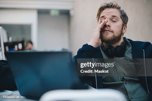 Tired computer programmer rubbing eyes while sitting in office Tired computer programmer rubbing eyes while sitting in office