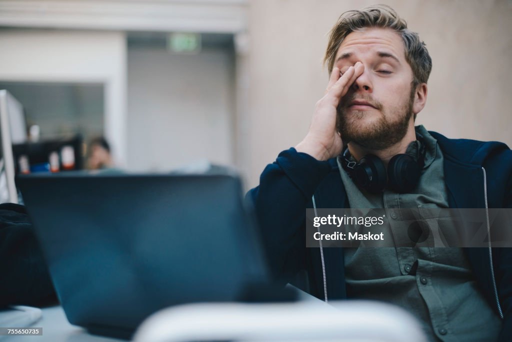 Tired computer programmer rubbing eyes while sitting in office