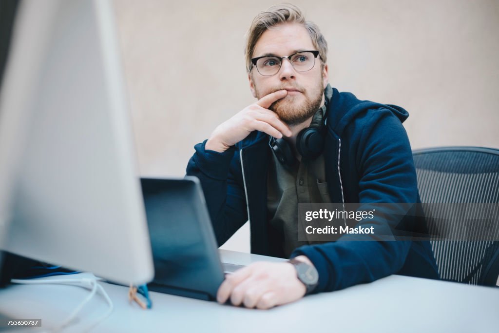 Thoughtful computer programmer sitting at desk in office