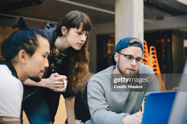 male and female computer programmers using laptop at desk in office - webdesigner stockfoto's en -beelden