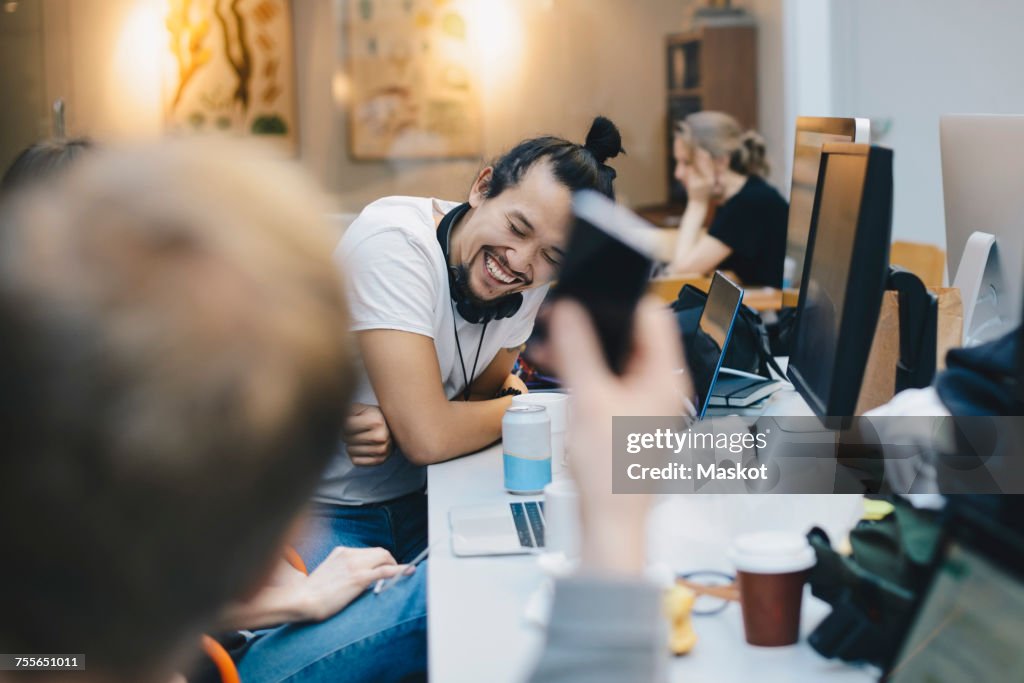 Happy computer programmer sitting with colleagues at desk in office