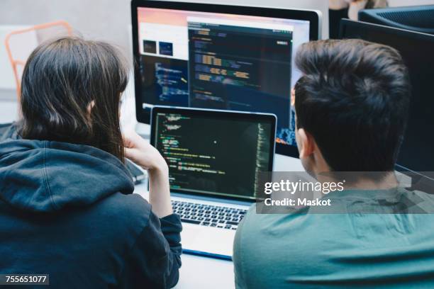 rear view of computer programmers using laptop at office desk - web designer fotografías e imágenes de stock