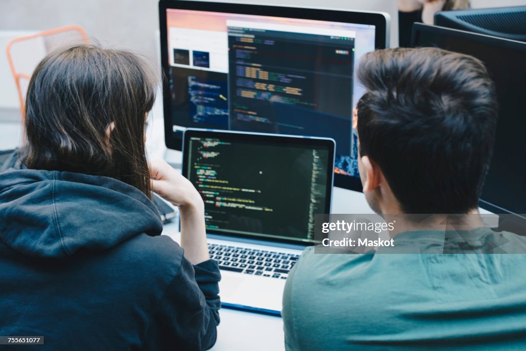 Rear view of computer programmers using laptop at office desk