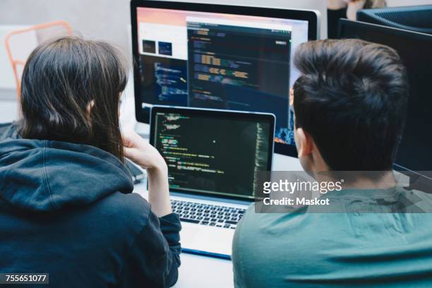 rear view of computer programmers using laptop at office desk - webdesigner stockfoto's en -beelden