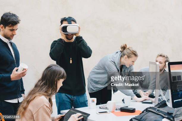 male computer programmer using vr glasses while colleagues working in office - casques réalité virtuelle photos et images de collection
