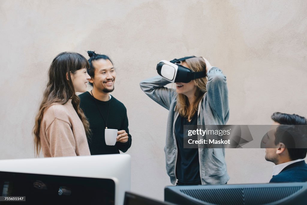 Happy computer programmer wearing VR glasses while talking to colleagues in office