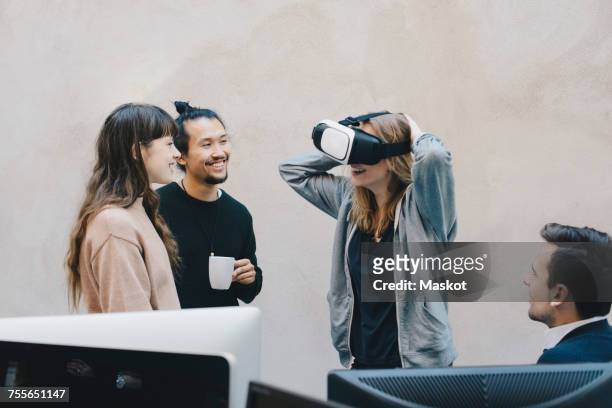 happy computer programmer wearing vr glasses while talking to colleagues in office - four people office stock pictures, royalty-free photos & images