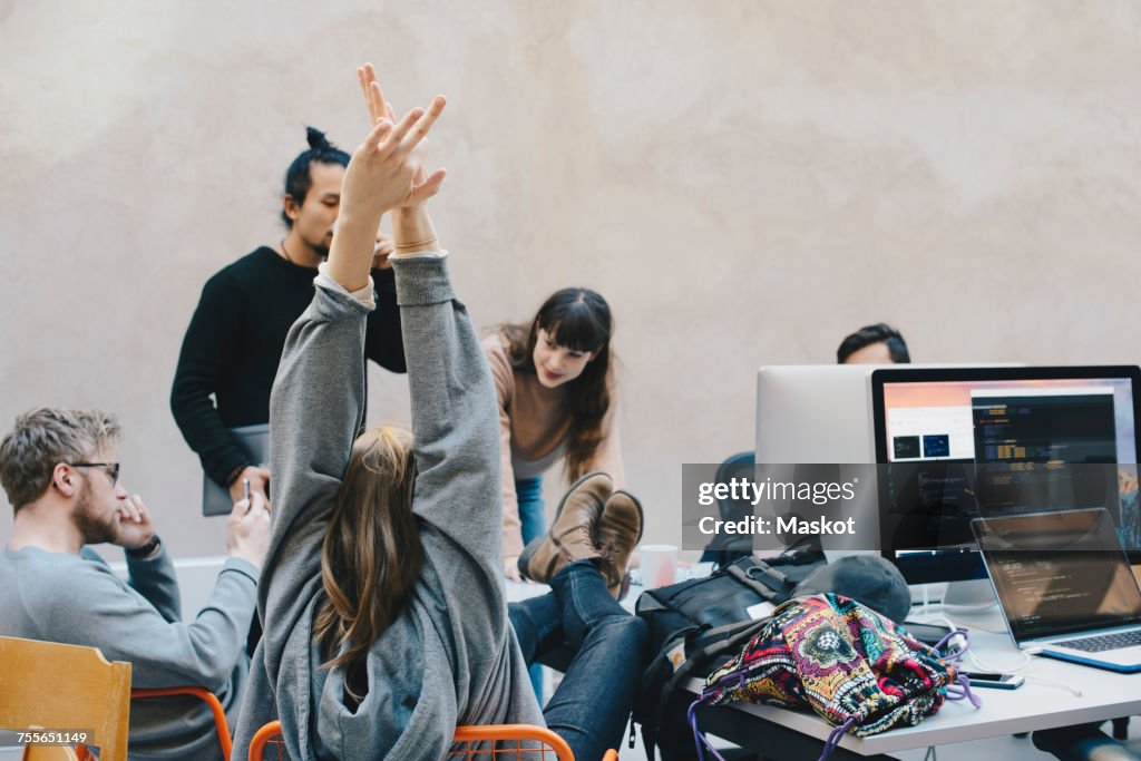 Rear view of female computer programmer stretching arms while sitting with colleagues in creative office