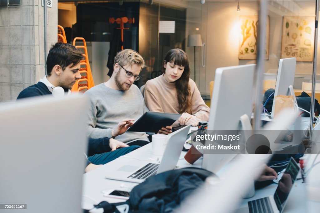 Male and female computer programmers using digital tablet at desk in office