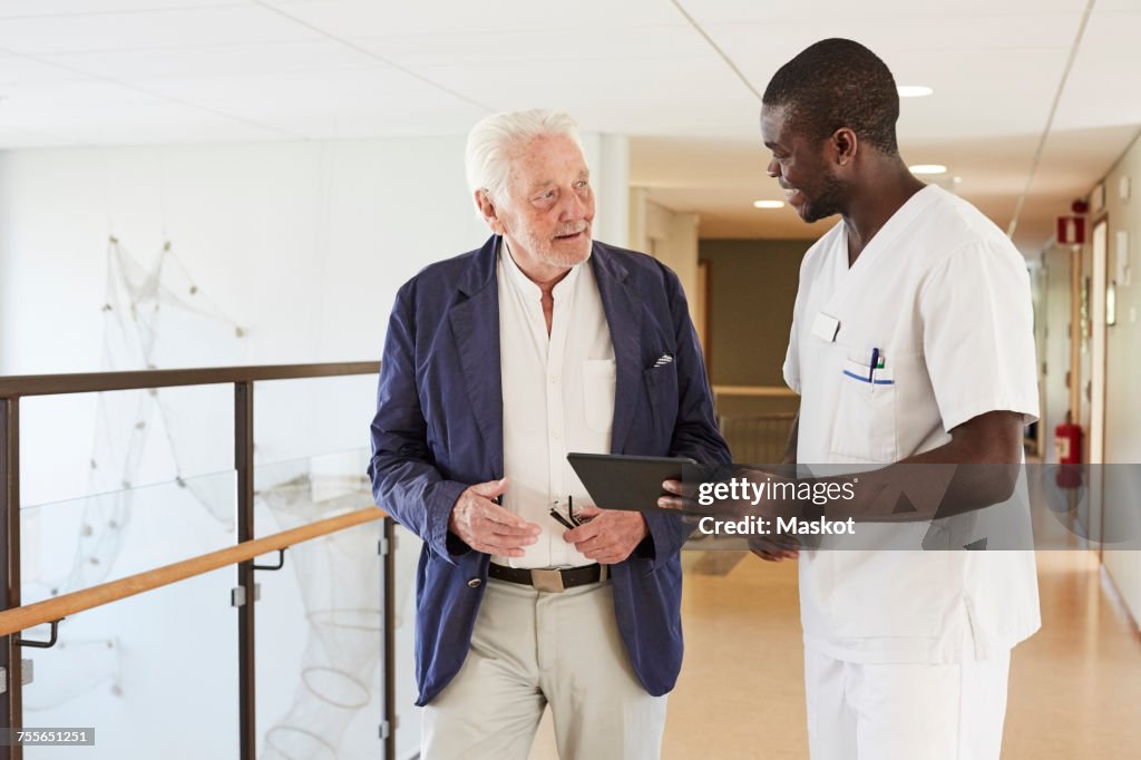 Male nurse and senior male patient discussing over digital tablet at hospital corridor