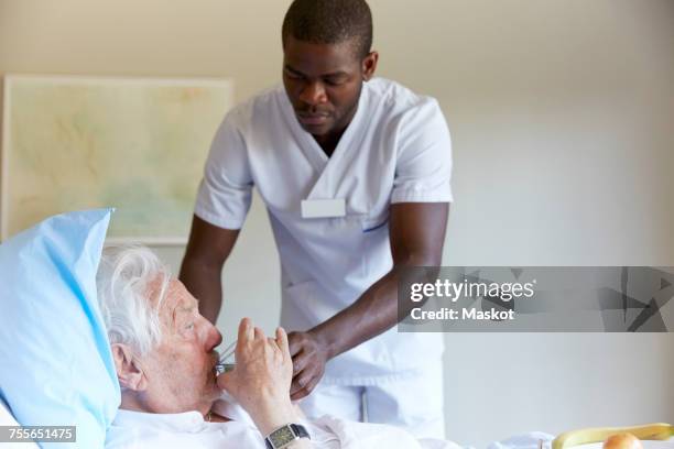 male nurse feeding water to senior man in hospital ward - nurse with old male patient home care stock-fotos und bilder