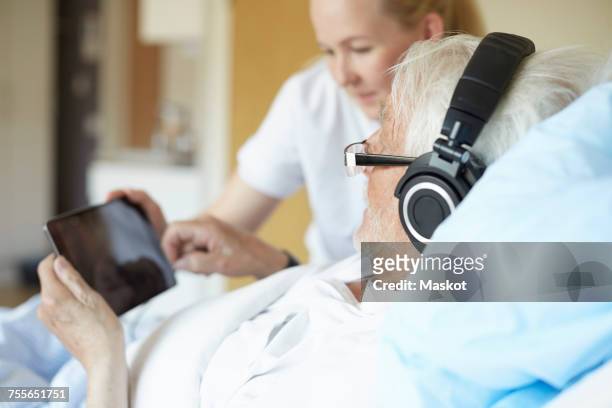 senior man wearing headphones while using digital tablet with female nurse on hospital bed - pillow icon stock pictures, royalty-free photos & images