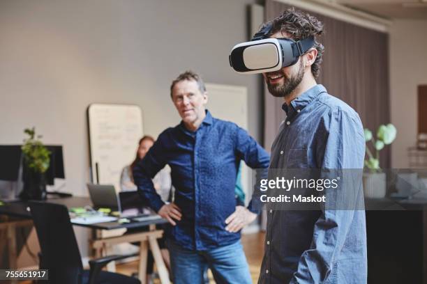 mature businessman looking at male colleague using virtual reality simulator while standing in creative office - virtual bildbanksfoton och bilder