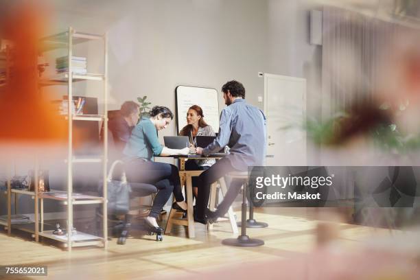 business professionals are discussing while sitting with laptops at desk in creative office - 50 sombras fotografías e imágenes de stock