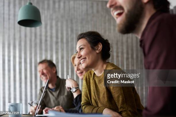 cheerful creative business colleagues sitting at conference table while looking away in board room - geschäftsbesprechung stock-fotos und bilder