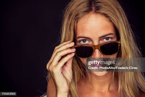 young woman peeking over top of sunglasses, portrait - gluren stockfoto's en -beelden